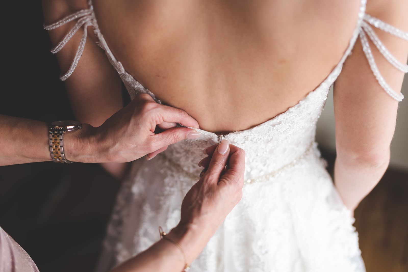 Hands adjust the back fastening of a formal dress during a fitting.